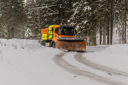Free A snow plow clearing a snow-laden road through a forest in Ettal, Germany. Stock Photo