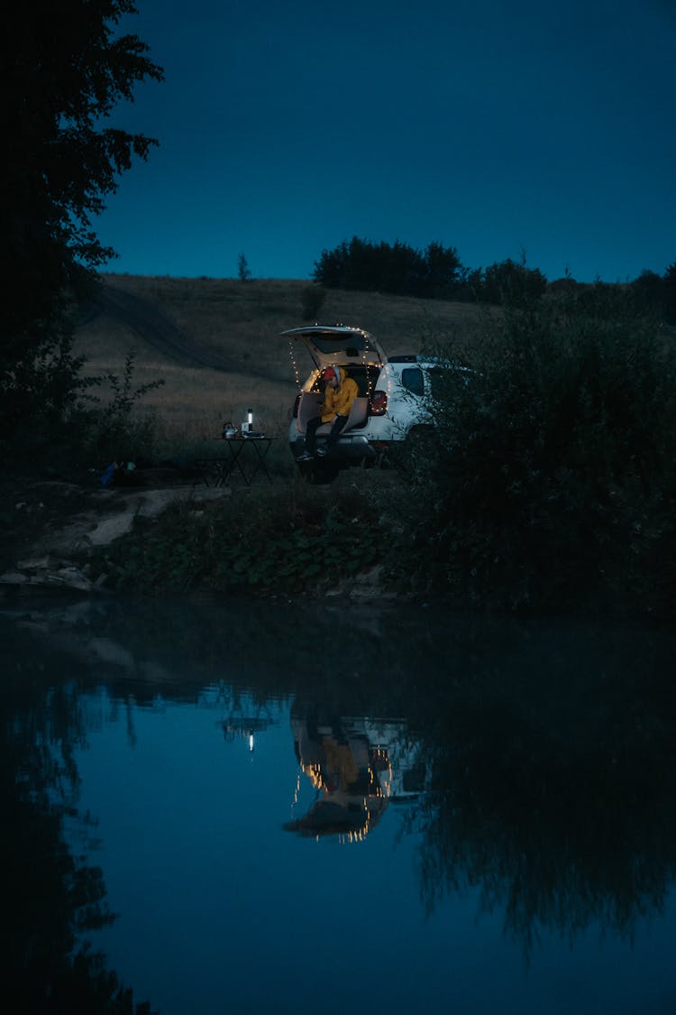 Person Sitting In Car Near Pond In Evening