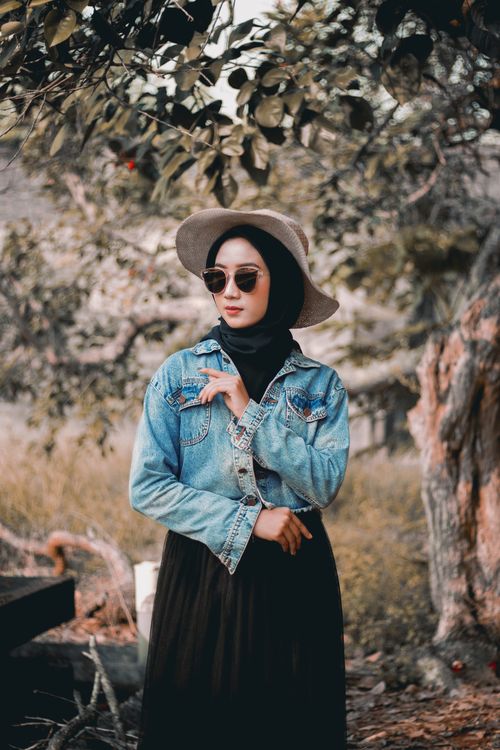 Free Fashionable woman wearing hijab and sunglasses posing outdoors with trees in the background. Stock Photo