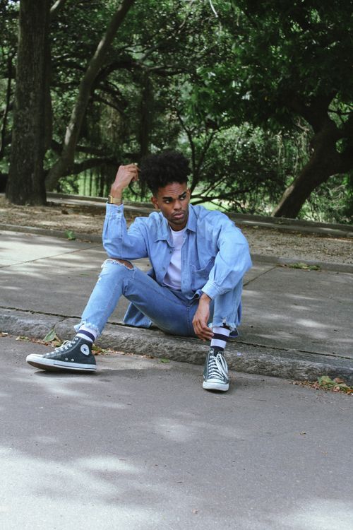 Free Fashionable man in denim outfit sitting on an outdoor sidewalk. Stock Photo