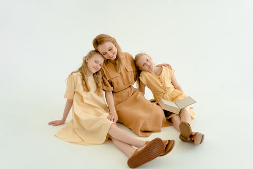 Free A joyful mother and her two daughters smiling and sitting in a bright studio setting, sharing a book. Stock Photo