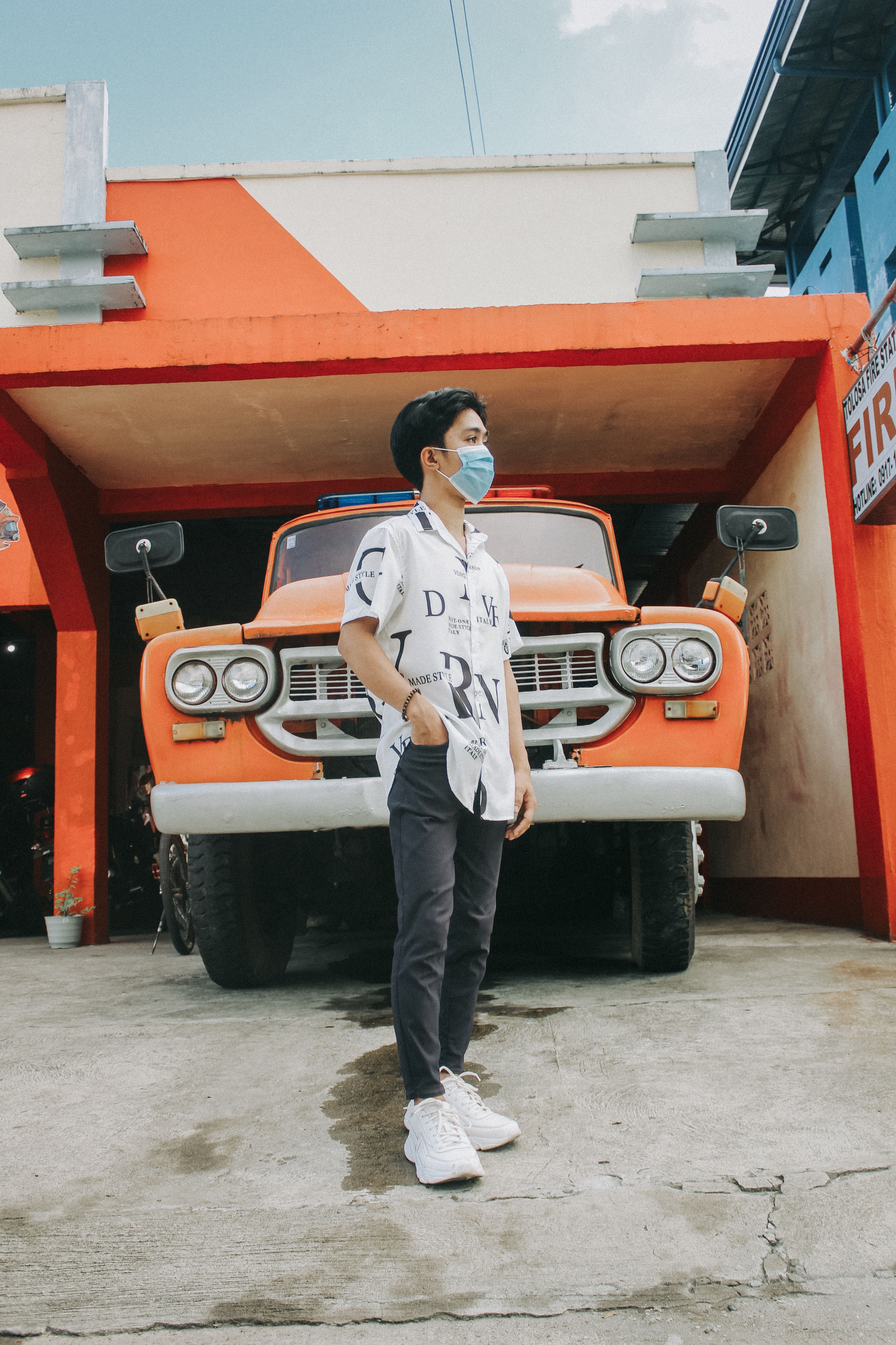 Young man with face mask standing in front of an orange vintage truck, representing new normal lifestyle.
