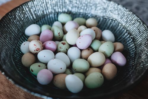 Free Close-up of multicolored candy eggs in a textured bowl on a wooden table. Stock Photo