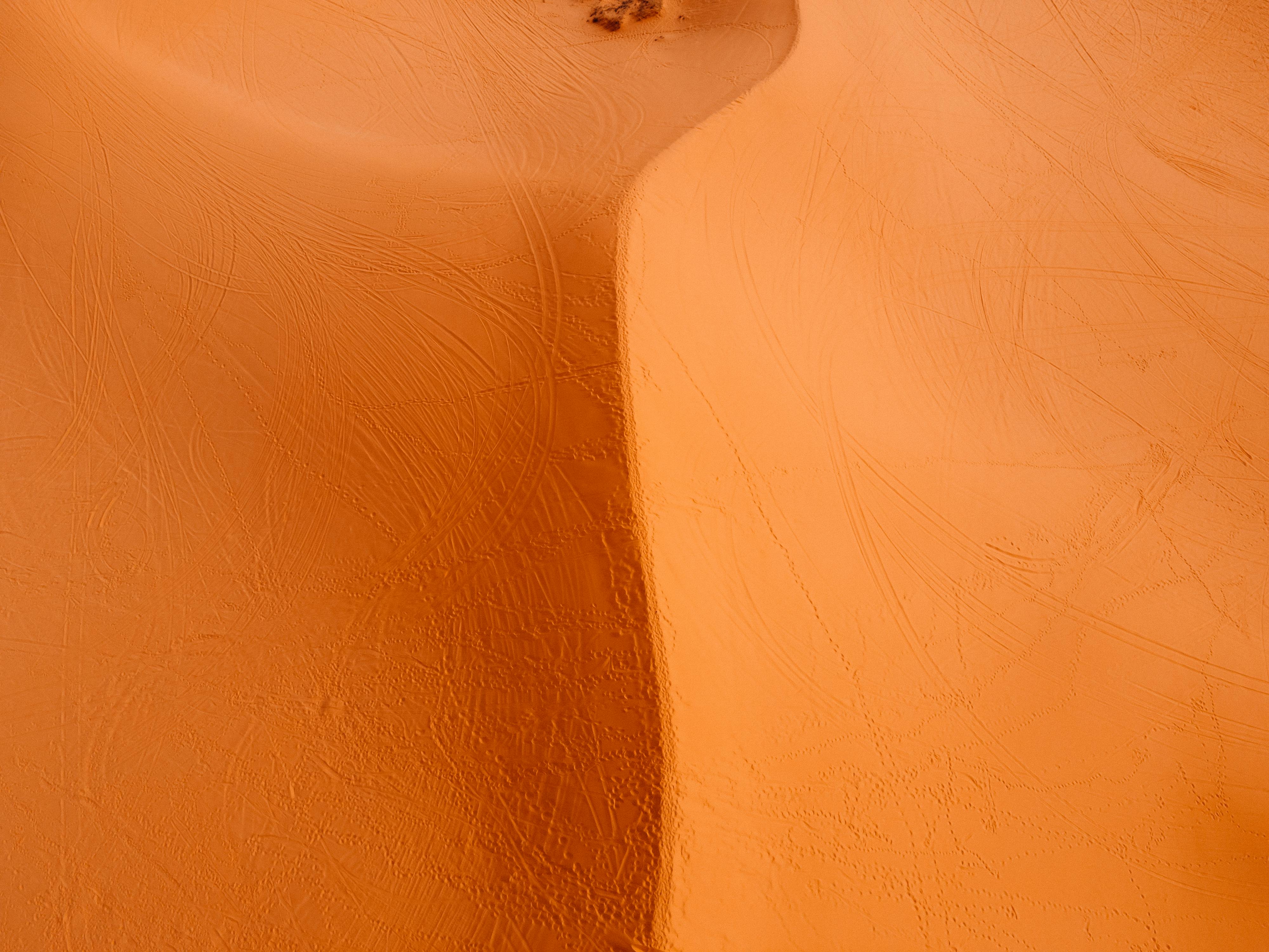 Sweeping aerial view of majestic sand dunes with visible tire tracks in Utah desert.