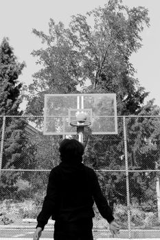 Grayscale photo of a person playing basketball, focusing on the hoop.