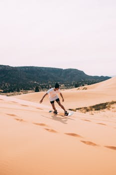 Young person sandboarding on Utah's dunes with scenic desert backdrop.