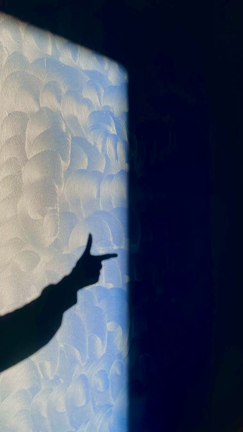 A Light Casting a Shadow on the Wall of a Person Doing a Finger Gun