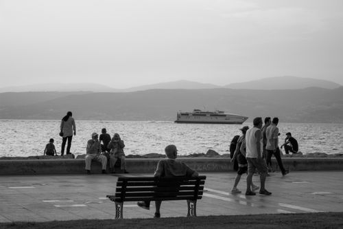 Free A serene grayscale scene of people relaxing by the harbor with a passing ferry in view. Stock Photo