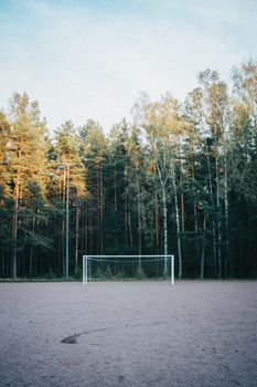 A solitary soccer goal stands in an open field, framed by lush green forest trees under a clear sky.