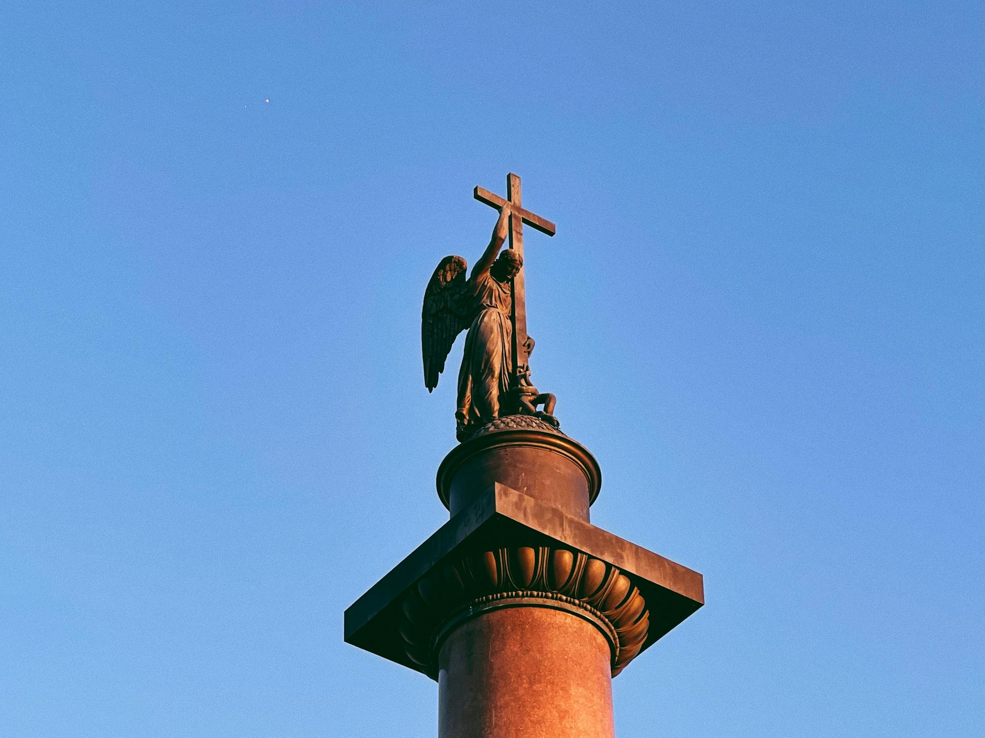 Angel sculpture holding a cross atop the Alexander Column under a vivid blue sky in Saint Petersburg.