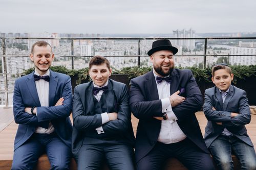 Free Four males in suits celebrating a special occasion with laughter on a rooftop. Stock Photo