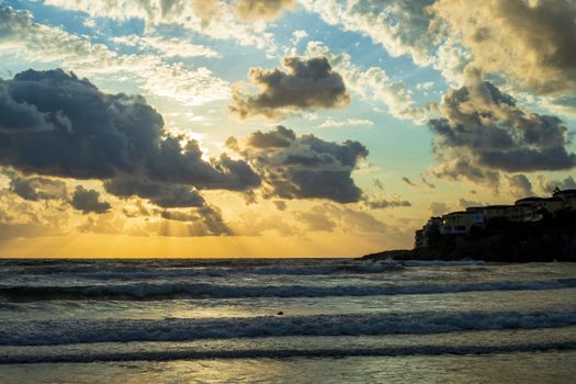 Stunning ocean sunset with dramatic clouds casting golden rays over the sea waves.