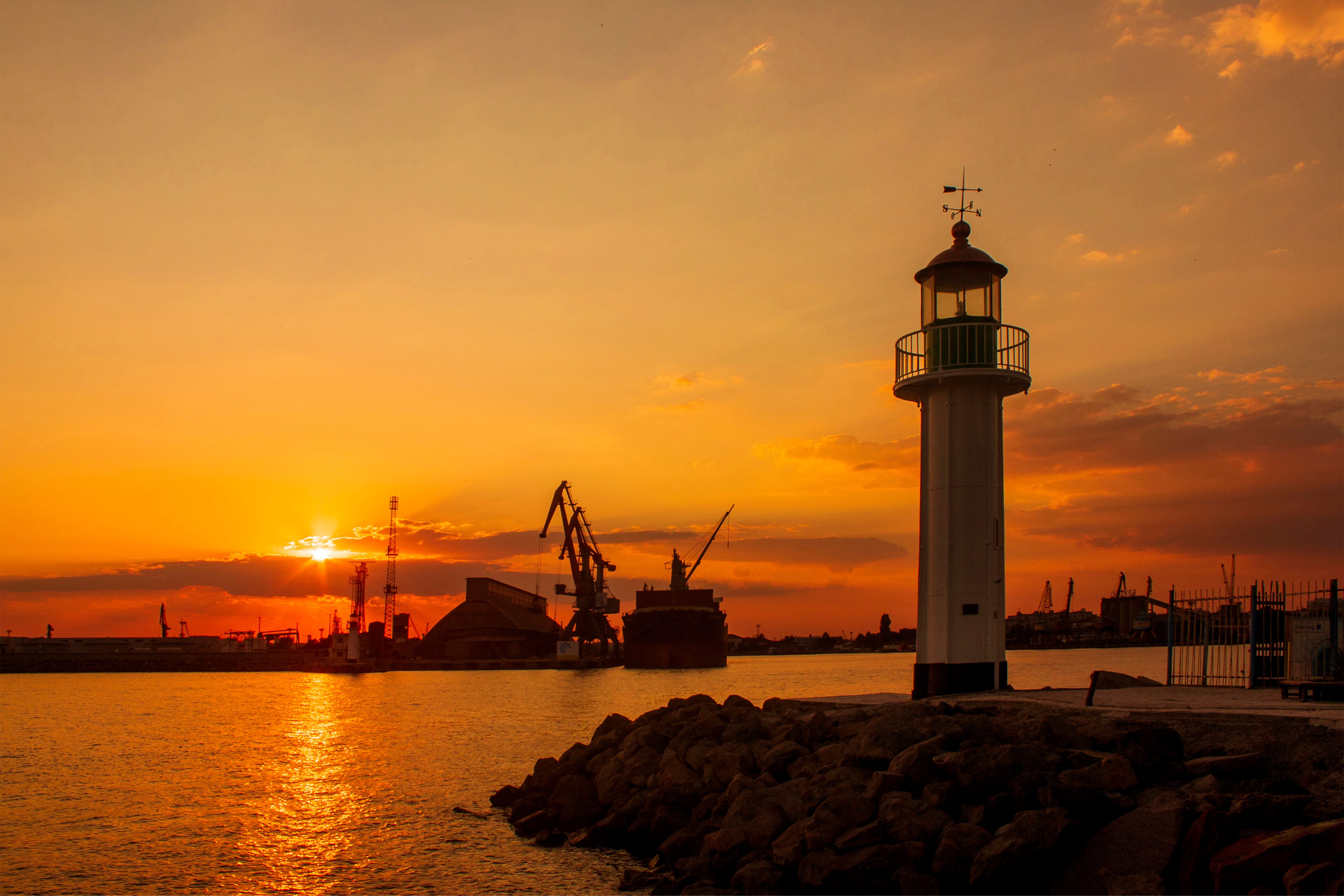 A scenic sunset with a lighthouse silhouette on the edge of a harbor, evoking tranquility.