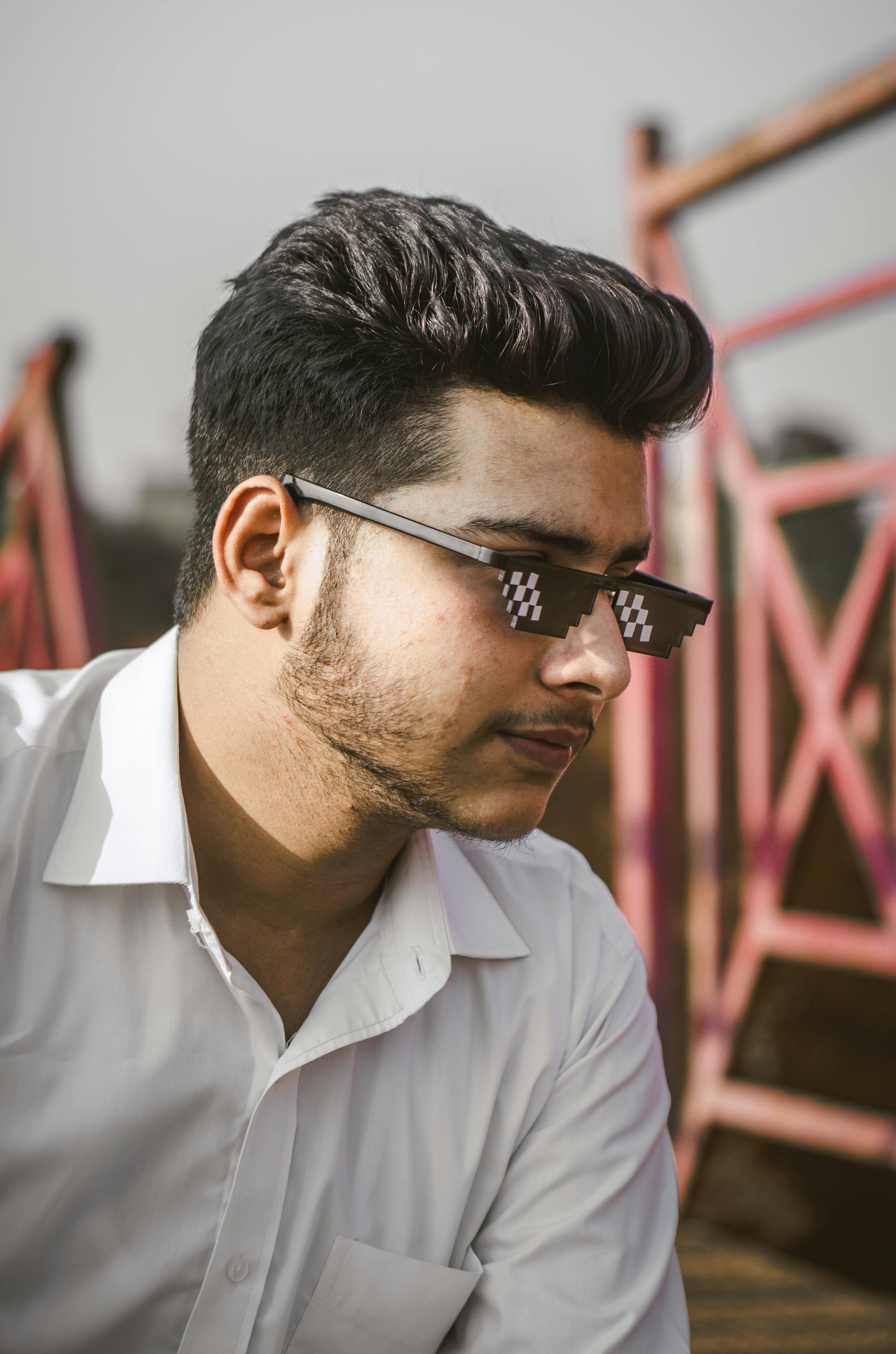 A young man wearing trendy pixelated sunglasses and a white shirt outdoors.