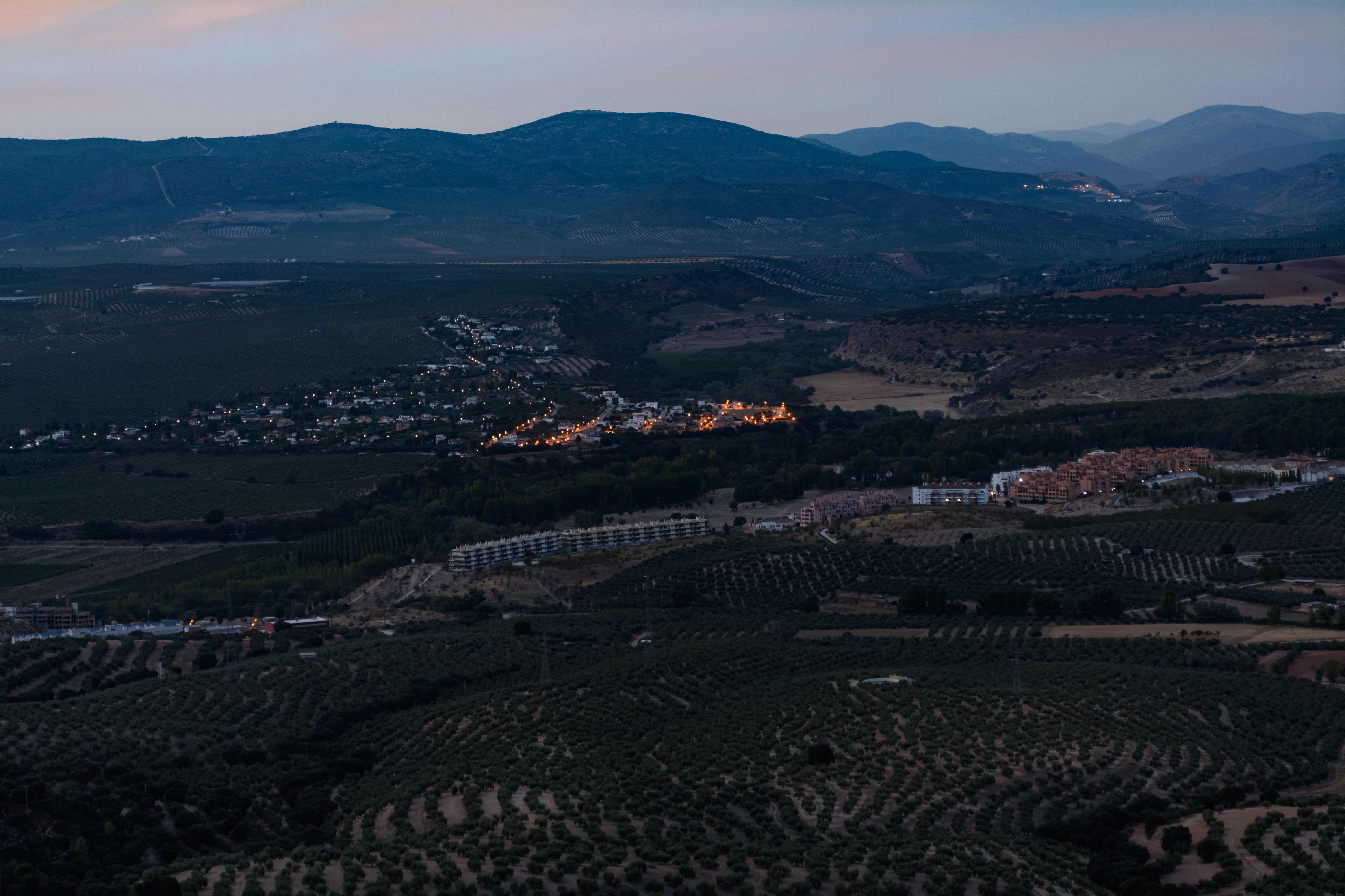 Dusk aerial view of a village surrounded by agricultural fields and mountains.