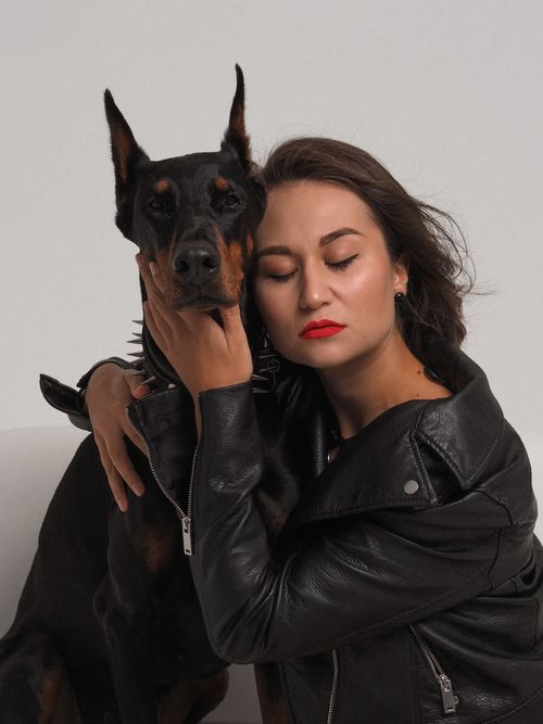 Free A touching studio portrait of a woman in a leather jacket embracing a Doberman dog. Stock Photo