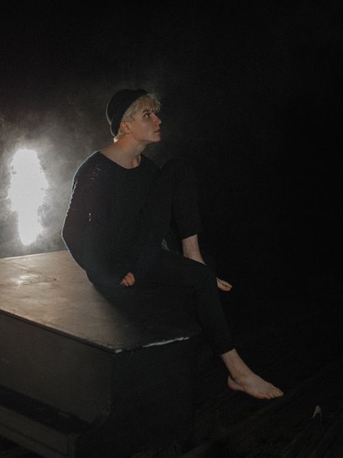Free A thoughtful young man sits barefoot in the dark, lit softly from the side, evoking introspection. Stock Photo