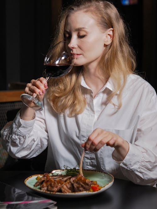 A Woman in White Long Sleeves Eating and Drinking Red Wine