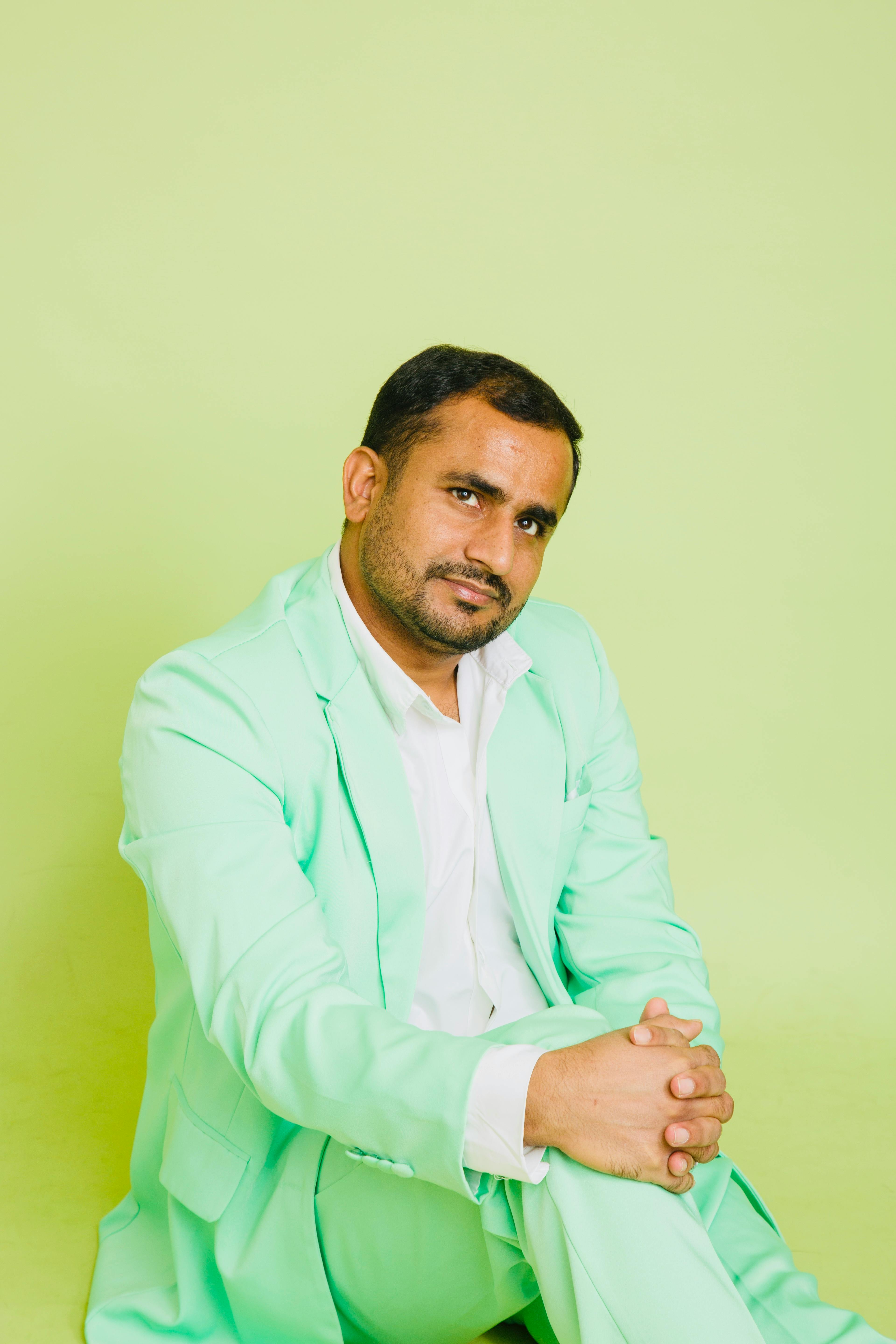 A man in a light green suit posing confidently against a green background indoors.