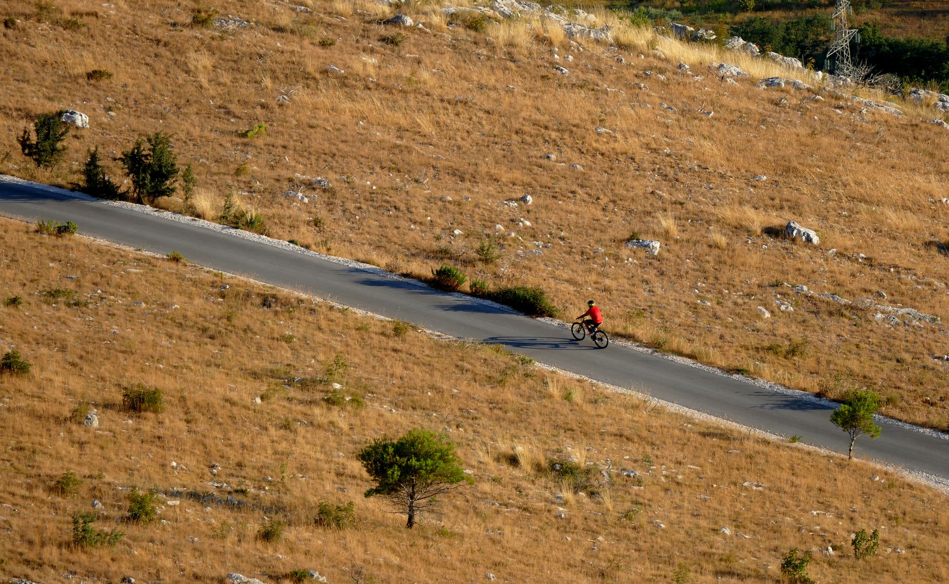 Aerial view of a cyclist riding on a rural road through dry grasslands in Croatia.