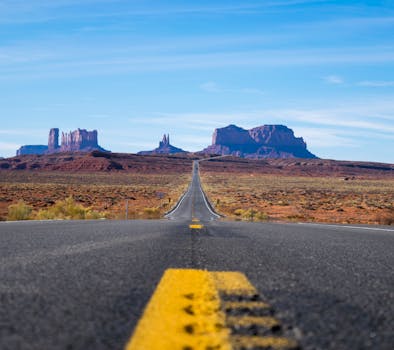 在晴朗的蓝天下，一条笔直的高速公路穿过标志性的纪念碑谷