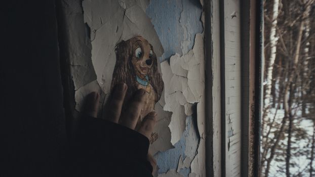 A human hand touching an old wall with peeling paint and a cartoon dog drawing.