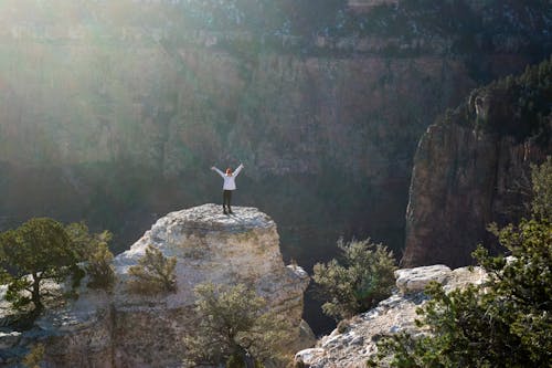 Vrouw In Witte Jas En Zwarte Broek Staande Op Brown Rock Formation Mountain