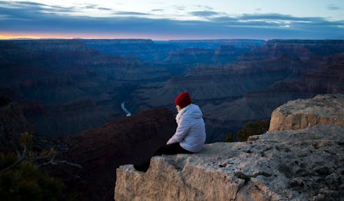 Person Wearing White Hoodie Sitting on Cliff at Daytime