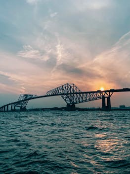An iconic bridge silhouetted against a vibrant sunrise over the water, showcasing structural beauty and serenity.