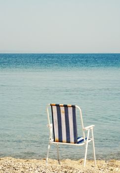Relaxing beach scene with a folding chair facing the calm blue ocean on a sunny day.