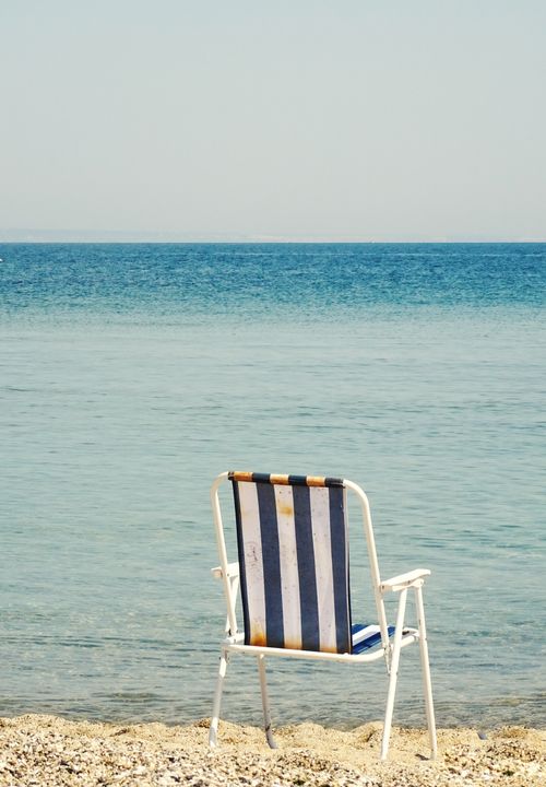 Free Relaxing beach scene with a folding chair facing the calm blue ocean on a sunny day. Stock Photo