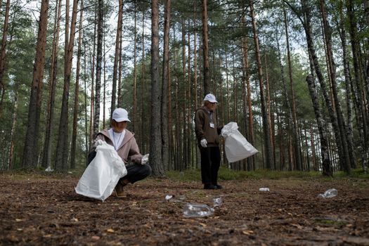 Two volunteers picking up trash in a forest to protect the environment.
