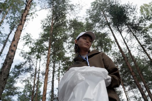 Woman picking up litter in a forest, promoting environmental awareness.