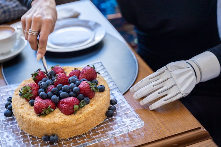 A Person With Prosthetic Arm Cutting The Cake