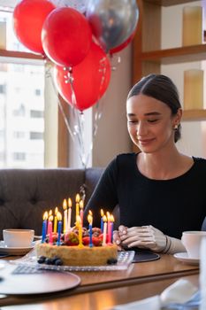 A woman with a prosthetic arm enjoys a birthday celebration indoors with balloons and cake.