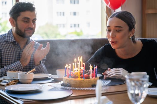 A joyful celebration with friends as a woman blows out birthday cake candles, creating a festive moment.