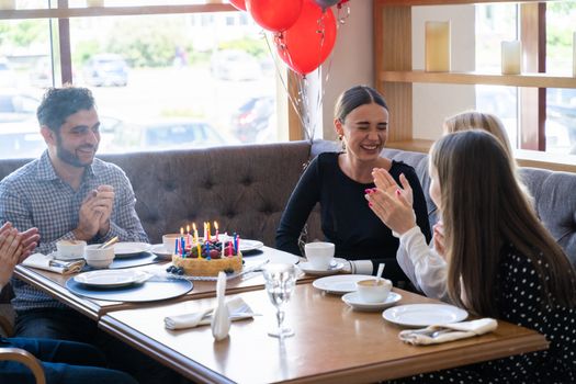 Friends celebrate a birthday with cake and laughter at a cozy restaurant setting.