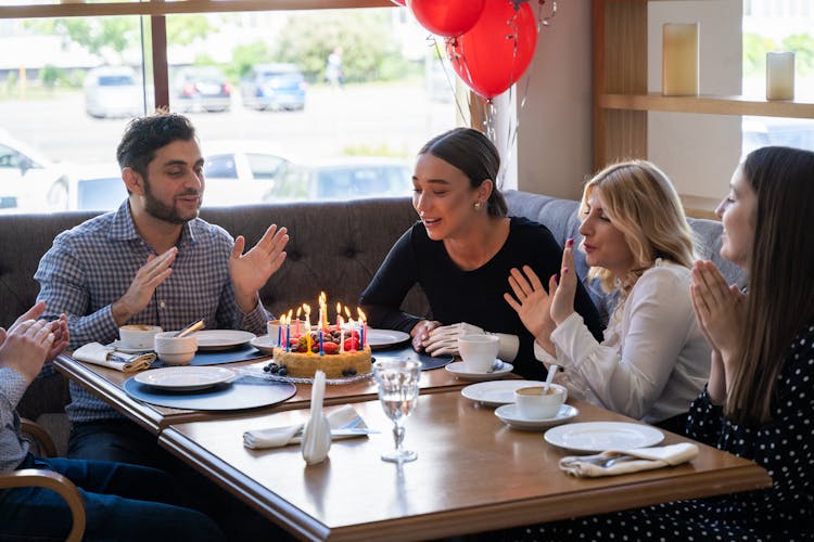 People Sitting At Table With Birthday Cake
