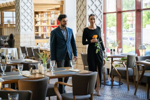 A sophisticated couple walks gracefully inside a stylish restaurant, embracing romance and elegance.