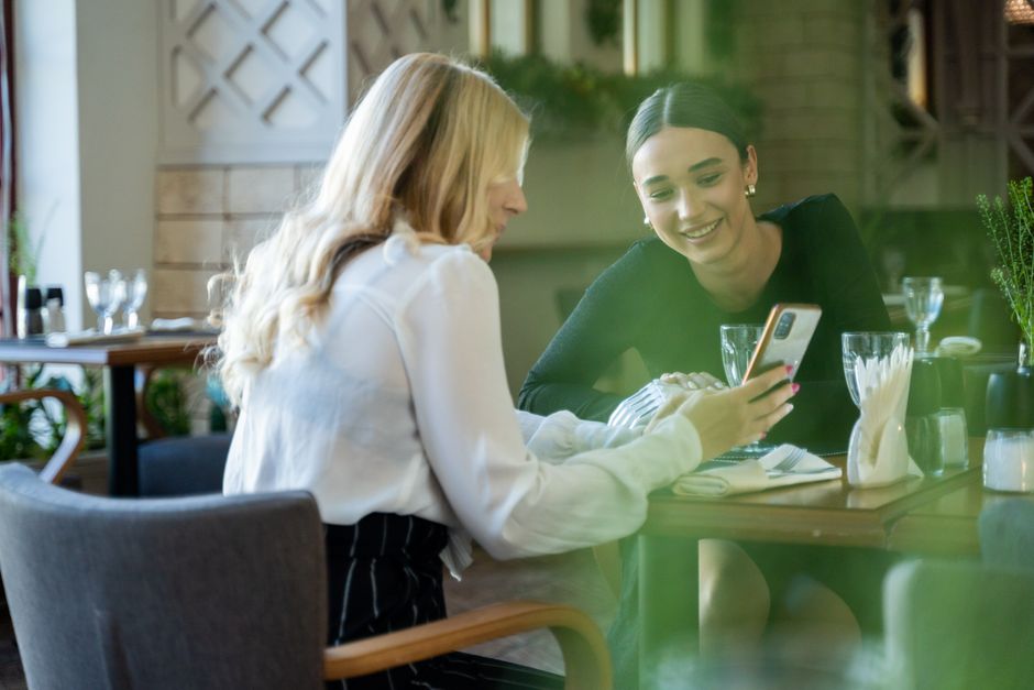 Friends using a phone together in a café, photographed by Mikhail Nilov on Pexels