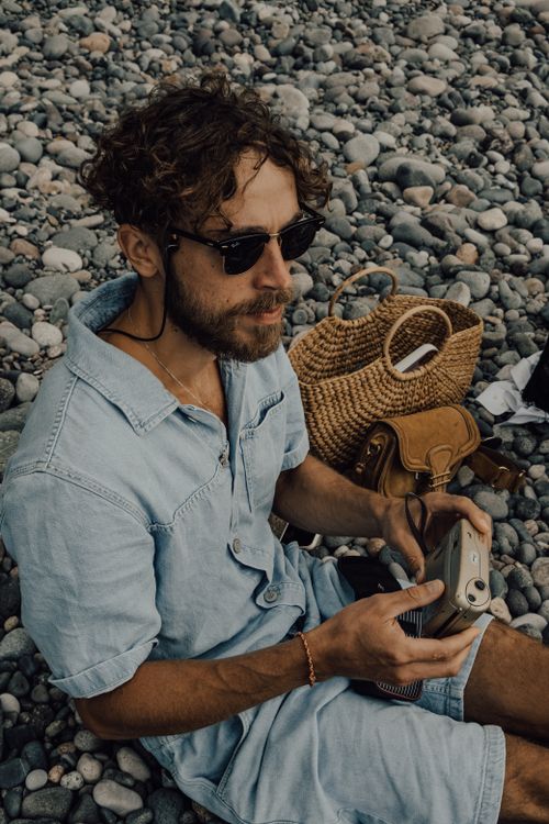 Free Casual man with sunglasses holding a camera while sitting on rocky beach in Batumi, Georgia. Stock Photo