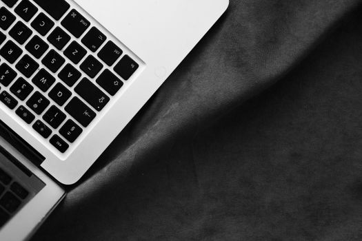 A minimalist black and white image of a laptop keyboard on a dark fabric surface.