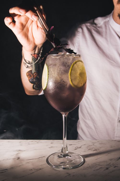 Free A bartender with a tattoo garnishes a cocktail with lime and herbs on a marble surface. Stock Photo