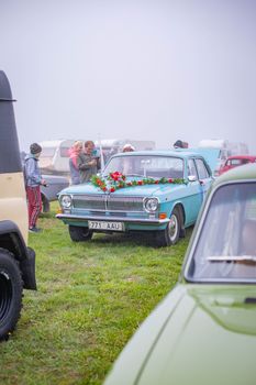 A classic light blue vintage car adorned with flowers on display outdoors during a car show.