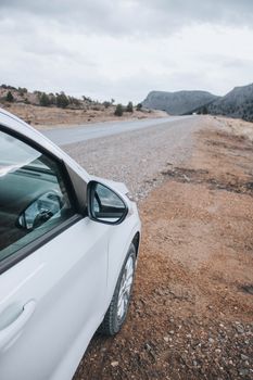 A white car is parked on a remote desert roadside under a cloudy sky.