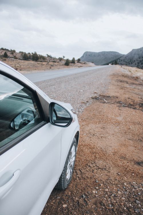 Free A white car is parked on a remote desert roadside under a cloudy sky. Stock Photo