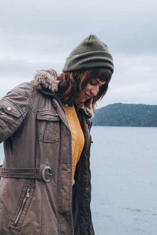 Free Woman wearing a jacket and beanie standing by a lake on a cool fall day. Stock Photo