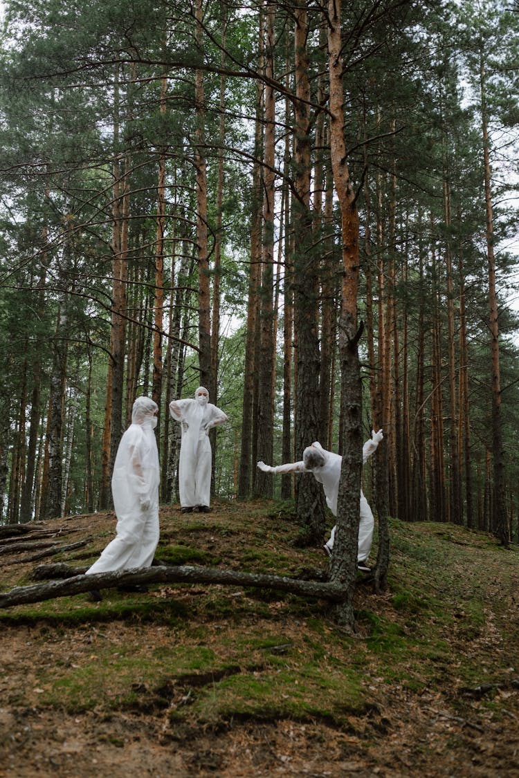 Three People Wearing White Hazmat Suits In The Woods