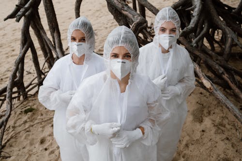 Group of Women Standing on a Beach in White Gowns and Face Mask 