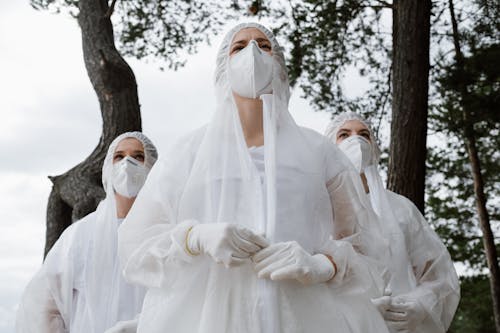 Group of Women Standing in a Forest in White Gowns and Face Mask 